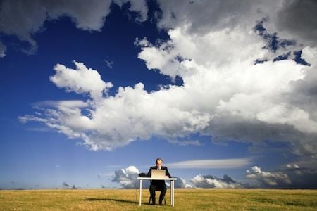 Blue sky beeminding person at a desk in the middle of a field with a big blue sky